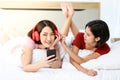 Happy Couple  asia woman wear headphones and enjoy musics playing mobile phone and tablet in bedroom Royalty Free Stock Photo