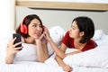 Happy Couple  asia woman wear headphones and enjoy musics playing mobile phone and tablet in bedroom Royalty Free Stock Photo