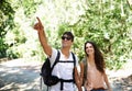 Happy couple, backpack and pointing with direction in forest for hiking, adventure or outdoor journey in nature. Young Royalty Free Stock Photo