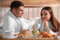 Happy couple in bathrobes having breakfast on bed at home Royalty Free Stock Photo