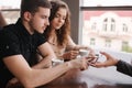 Happy couple in cafe look into smartphone and smile. Woman show to man and woman something in phone. Man put finger on Royalty Free Stock Photo