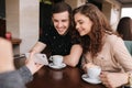 Happy couple in cafe look into smartphone and smile. Woman show to man and woman something in phone. Man put finger on Royalty Free Stock Photo