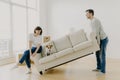 Happy couple carry modern white sofa with dog together, place furniture in living room, care about improvement of interior design Royalty Free Stock Photo