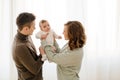 Happy couple carrying adorable baby near curtain