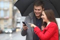 Happy couple checking phone in winter under rain