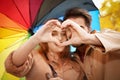 Happy couple with colorful umbrella making heart with hands