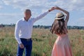 happy couple dancing in the field. brunette in cream dress and bald man in white shirt and blue pants. love story Royalty Free Stock Photo