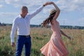 happy couple dancing in the field. brunette in cream dress and bald man in white shirt and blue pants. love story