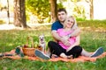 Happy Couple With Dog Sit On Orange Picnic Blanket