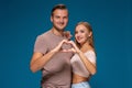 Happy couple dressed casual clothes, making heart shape from fingers, studio portrait on blue background Royalty Free Stock Photo