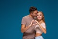 Happy couple dressed casual clothes, making heart shape from fingers, studio portrait on blue background Royalty Free Stock Photo