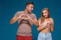 Happy couple dressed casual clothes, making heart shape from fingers, studio portrait on blue background Royalty Free Stock Photo