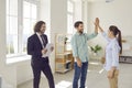 Happy couple giving high five each other buying a house standing with smiling man realtor. Royalty Free Stock Photo