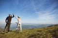 Happy couple goes on a mountain asphalt road in the woods on bikes with helmets giving each other a high five Royalty Free Stock Photo