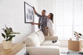 Happy couple hanging picture on white wall together. Interior design