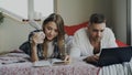 Happy couple have rest at home. Young man and woman lying in bed reading book and using laptop computer in the morning Royalty Free Stock Photo