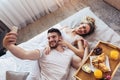 Happy couple having breakfast in luxury hotel room using smart phone to take selfie photo Royalty Free Stock Photo