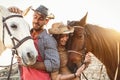 Happy couple having fun with horses inside stable - Young farmers sharing time with animals in corral ranch Royalty Free Stock Photo