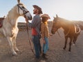 Happy couple having fun with horses inside stable - Young farmers sharing time with animals in corral ranch Royalty Free Stock Photo