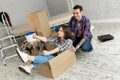 Happy couple having fun laughing moving into new home, young excited woman riding sitting in cardboard box while man Royalty Free Stock Photo