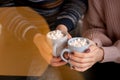 Happy couple`s hands holding hot cups with hot drinks with marshmallow Royalty Free Stock Photo