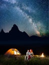 Happy couple hikers covered with a plaid sitting together under starry sky near campfire and camp at night Royalty Free Stock Photo