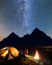 Happy couple hikers sitting face to face in front tent near campfire under shines starry sky at night Royalty Free Stock Photo