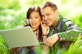 Happy couple of hipsters in trendy casual clothing using a laptop with earphones in park forest, garden and looking sweet and