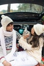 Happy couple holding a fluffy rabbit in the back of car with Christmas gift box in winter forest. Royalty Free Stock Photo