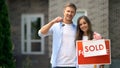 Happy couple holding keys from house near sold sign, mortgage for young families Royalty Free Stock Photo