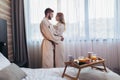 Happy couple in hotel room in the morning. Just married man and woman standing at window