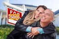 Happy Couple Hugging in Front of Sold Real Estate Sign and House Royalty Free Stock Photo