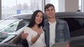 Happy couple hugging, holding car keys at dealership salon