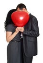 Happy couple kissing and hiding behind red heart shaped balloon. Valentine holiday concept. Studio isolated