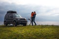 Happy couple kissing and hugging standing on the top of the mountain. Car trip on SUV with roof rack, trip at summer day. Man and Royalty Free Stock Photo
