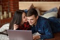 Happy couple with laptop shopping online at home, browsing internet in bed, smiling and having fun Royalty Free Stock Photo