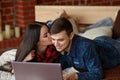 Happy couple with laptop spending time together at home, browsing internet in bed, smiling and having fun Royalty Free Stock Photo