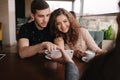 Happy couple in cafe look into smartphone and smile. Woman show to man and woman something in phone. Man put finger on Royalty Free Stock Photo