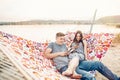 Happy couple looking at phones and smiling, relaxing in hammock in sunset light on the beach. stylish hipsters having fun, and