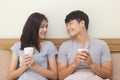 Asian young man and woman holding coffee cup on the bed. The lover smile and look at each other face happily Royalty Free Stock Photo