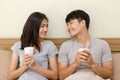 Asian young man and woman holding coffee cup on the bed. The lover smile and look at each other face happily Royalty Free Stock Photo