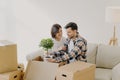 Happy couple in love settle in new home, unpack boxes with household objects, man holds potted plant, woman embraces and expresses Royalty Free Stock Photo