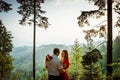 Happy couple in love is smiling and tenderly hugging in the forest at the background of the green mountains during the