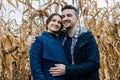 A happy couple in love stands in autumn near a cornfield. A man in a shirt and jacket hugs a woman in a coat