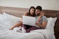 Happy couple lying on a bed with computer - Beautiful married couple watching sex video on laptop laughing together - People, Royalty Free Stock Photo