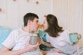 Happy couple lying in bed in cozy home, reading newspaper, drinking coffee. Young man in a t-shirt and a cute woman. Family Royalty Free Stock Photo