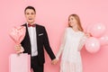 Happy couple, man and woman, with a bouquet of flowers and bags in their hands, after shopping, on a pink background. Trading Royalty Free Stock Photo