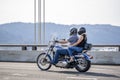 Happy couple man and woman in helmets ride a classic motorcycle on a cable bridge
