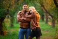 The happy couple, man and woman posing outdoor in the green autumn park in the red bomber leather coats