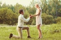 Happy couple, man kneeling down and proposing ring to his woman outdoors on the grass, wedding concept Royalty Free Stock Photo